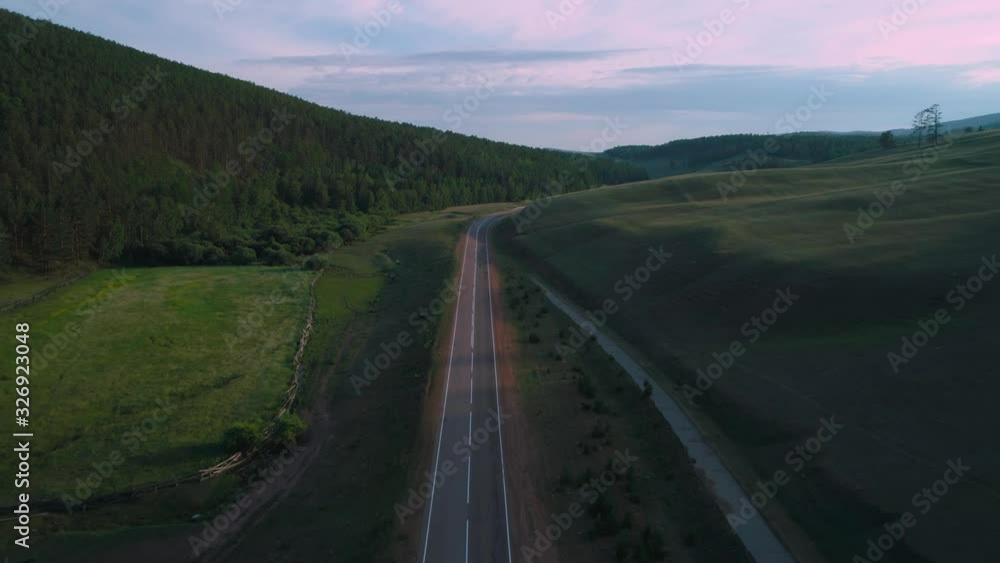 AERIAL, TOP DOWN: Dark colored car driving down an asphalt road crossing the vast forest on a sunny summer day. AERIAL, TOP DOWN: Dark colored car driving down an asphalt road crossing the vast forest on a sunny summer day.