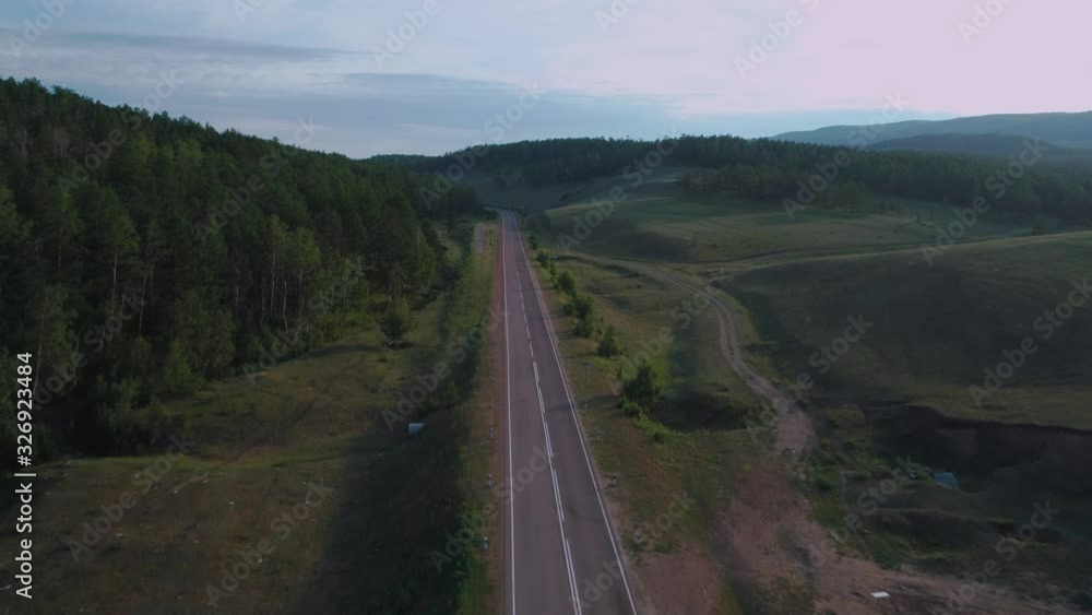 AERIAL, TOP DOWN: Dark colored car driving down an asphalt road crossing the vast forest on a sunny summer day. AERIAL, TOP DOWN: Dark colored car driving down an asphalt road crossing the vast forest on a sunny summer day.