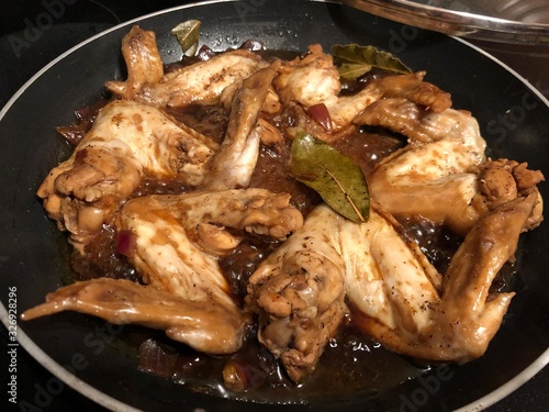 Chicken wings cooked adobo style in a pan, with bay leaves photo