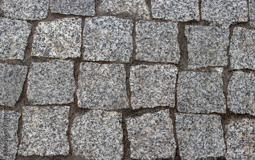 Granite cobblestoned pavement background. Cobbled stone road regular shapes, abstract background of old cobblestone pavement close-up