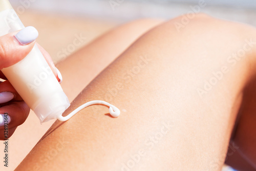 Closeup of female hand drawing something on her leg with sun cream sitting on the towel at the beach