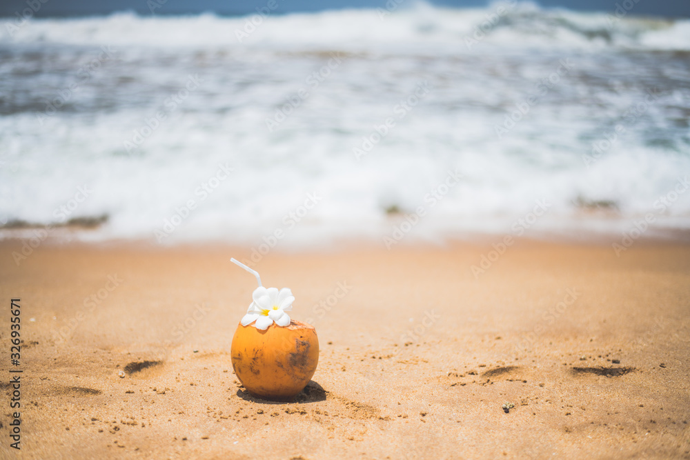 Obraz premium Fresh young orange coconut with a tube for drinks and Plumeria flowers in a tropical resort near the ocean
