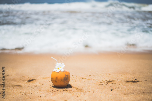 Fresh young orange coconut with a tube for drinks and Plumeria flowers in a tropical resort near the ocean
