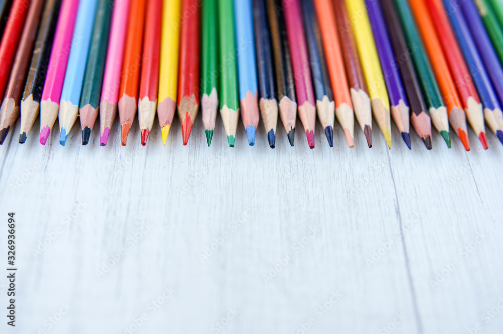 Multicolor sharpened pencils isolated on wooden background in a row Multicolor sharpened pencils isolated on wooden background in a row