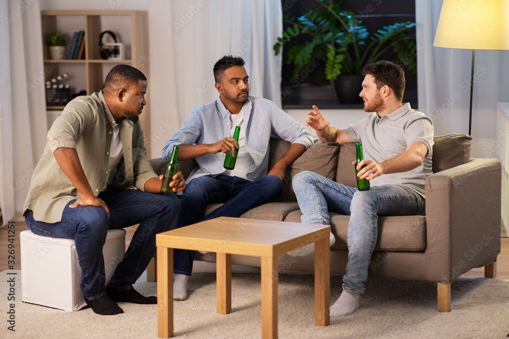 friendship, leisure and people concept - happy male friends drinking beer and talking at home at night
