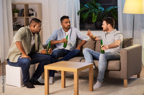 friendship, leisure and people concept - happy male friends drinking beer and talking at home at night