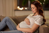 pregnancy and people concept - happy smiling pregnant woman on sofa at home