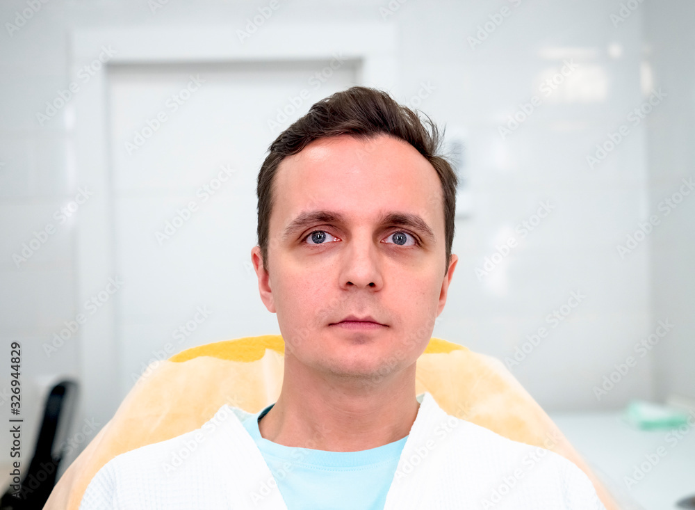 Beauty esthetics treatment. Waist up portrait of young brunette male in white bathrobe lying on couch ready for cosmetology procedure cosmetic center Beauty esthetics treatment. Waist up portrait of young brunette male in white bathrobe lying on couch ready for cosmetology procedure cosmetic center