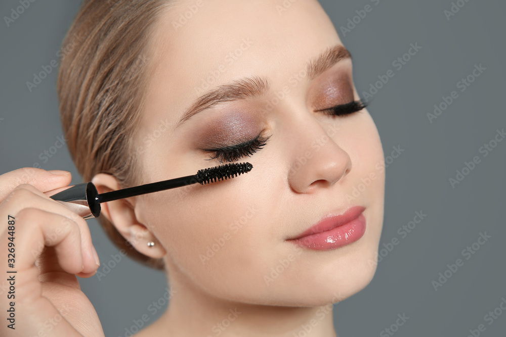 Beautiful woman applying mascara on light grey background. Stylish makeup