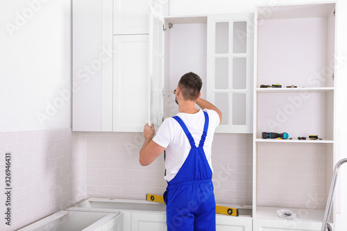 Worker installing door of cabinet with screwdriver in kitchen