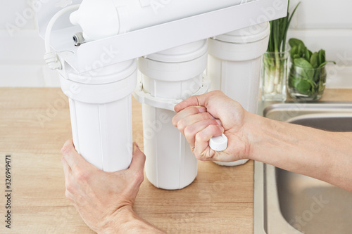 Plumber or man hand holding installation key and replace a water filter cartridges at home kitchen. Fix osmosis system.