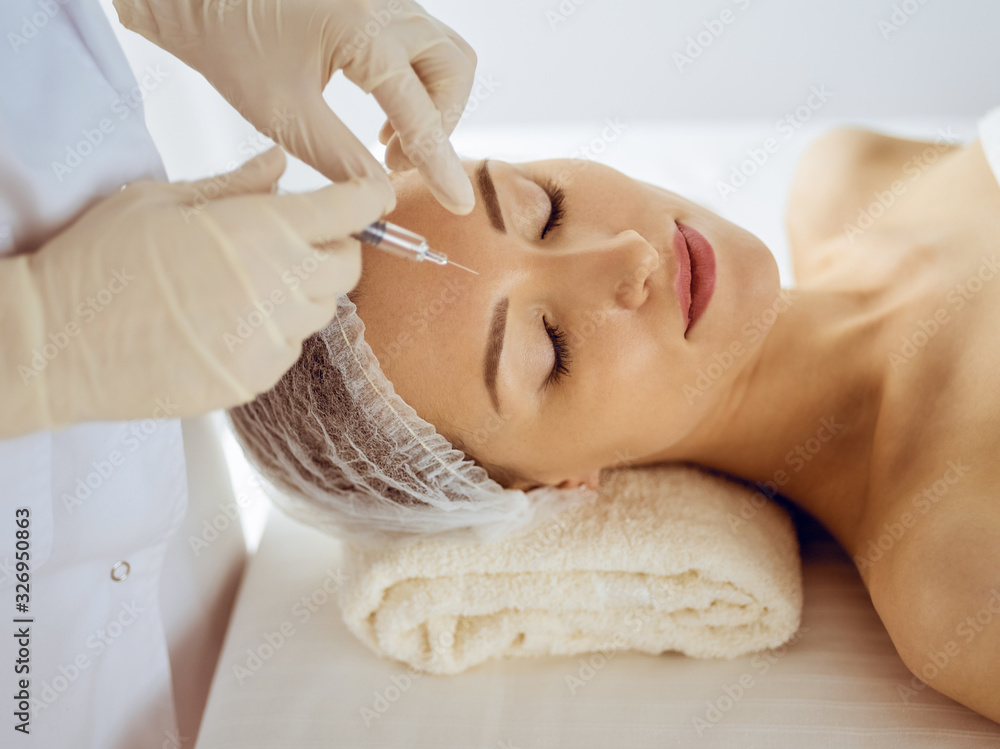 Beautiful woman receiving beauty injections with closed eyes. Beautician doctor hands doing beauty procedure to female face with syringe. Cosmetic medicine and surgery concept