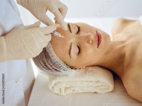Beautiful woman receiving beauty injections with closed eyes. Beautician doctor hands doing beauty procedure to female face with syringe. Cosmetic medicine and surgery concept