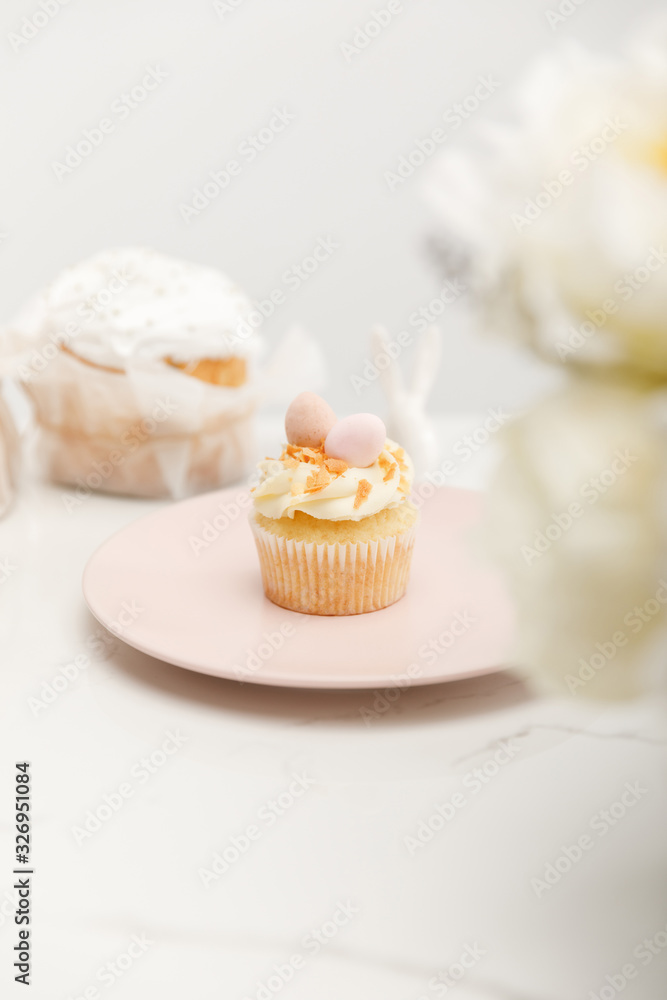 Selective focus of cupcake on plate and flowers on white background