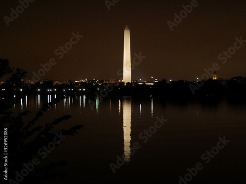 Medium wide shot of the Washington Monument with night lights of Washington, D.C. reflected in the waters of Potomac River.
