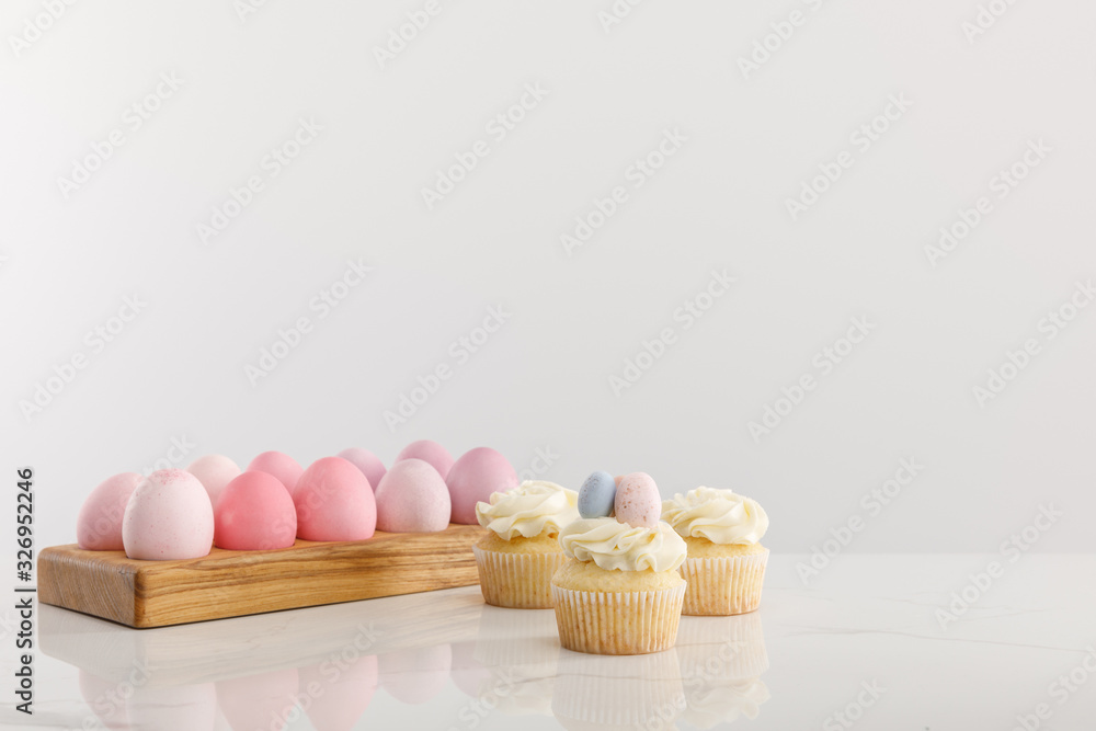 Easter eggs on egg tray with delicious cupcakes isolated on grey background Easter eggs on egg tray with delicious cupcakes isolated on grey background
