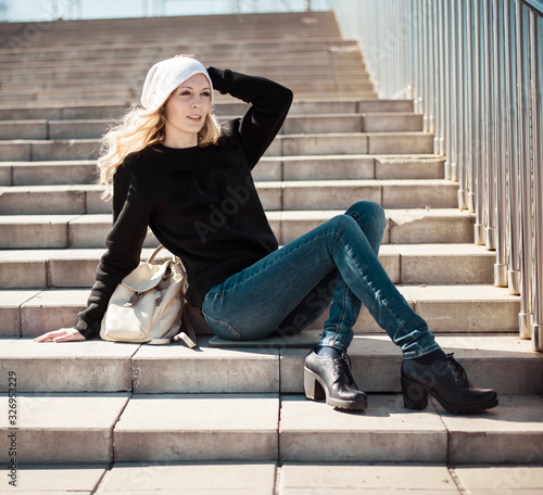 Fashion photo of a young beautiful woman in jeans, a black sweatshirt, a white knitted hat with a backpack © katafree