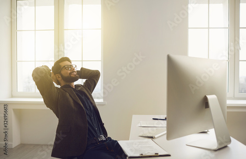 Businessman in glasses hands behind head contented dreams happy smiling sitting at a table in the office. photo