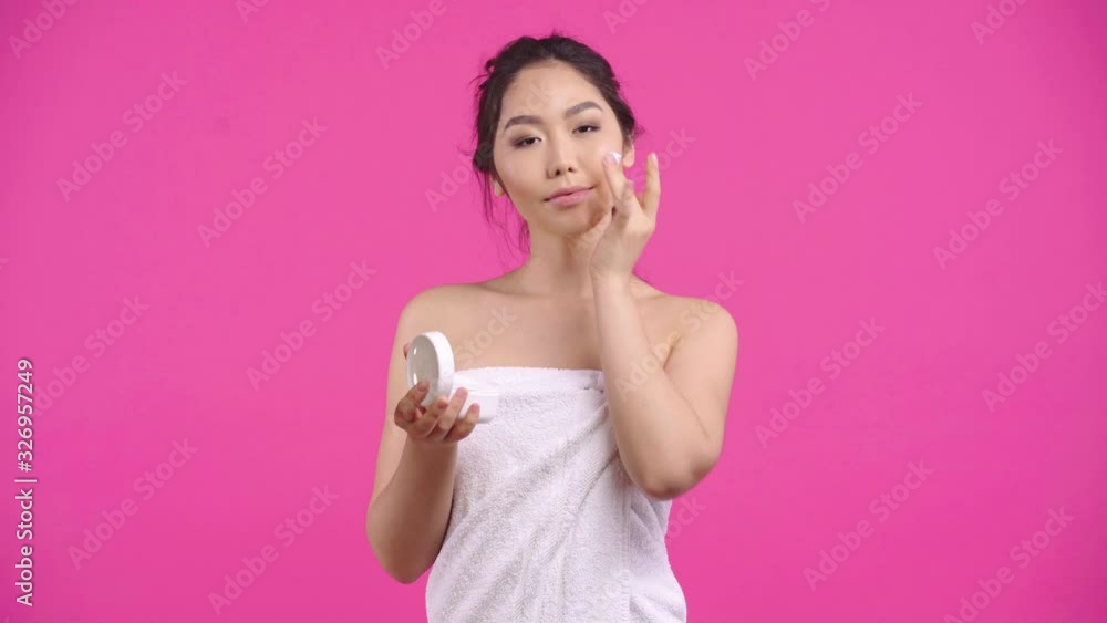 happy asian girl applying face cream isolated on pink happy asian girl applying face cream isolated on pink