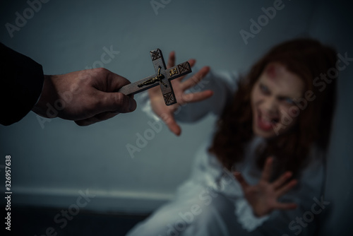 selective focus of exorcist holding cross in front of yelling obsessed girl