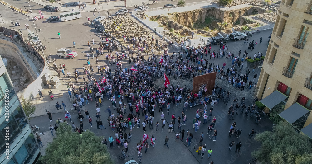 Fototapeta premium Beirut, Lebanon 2019: Aerial drone shot in Martyr's Square of numerous protesters trying to remove the wires blocking the road to the parliament with Phoenician ruins in the background