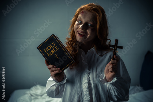 Valokuvatapetti smiling demoniacal woman holding cross and holy bible