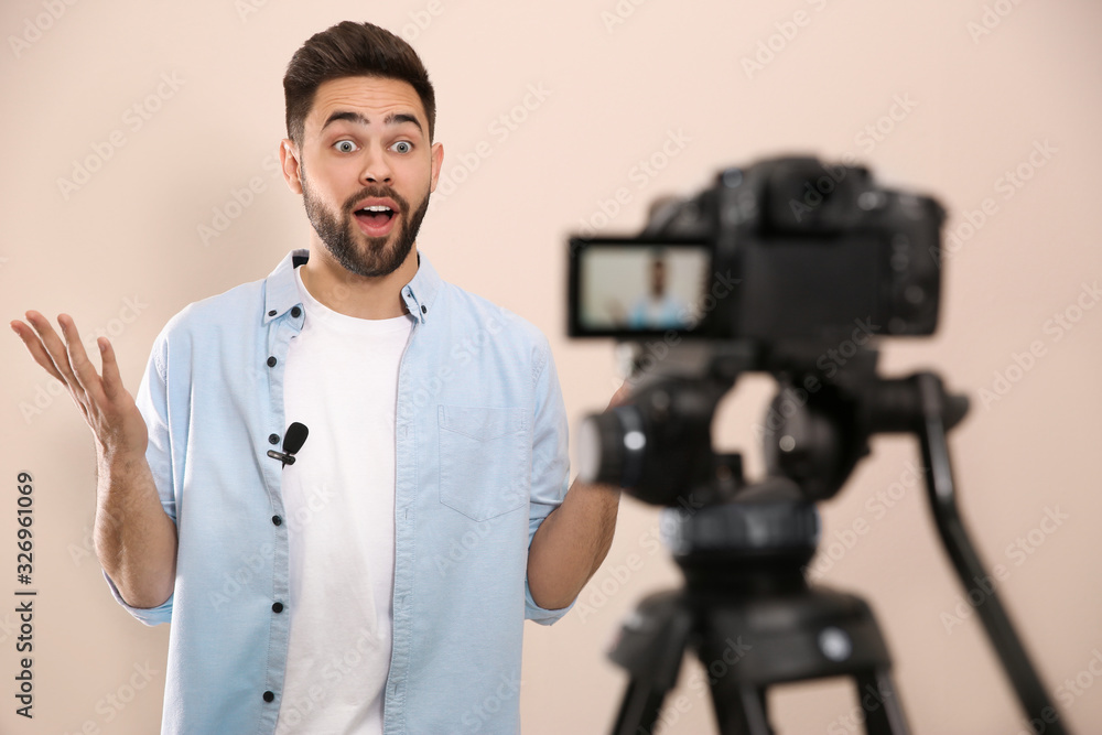 Young blogger recording video on camera against beige background Young blogger recording video on camera against beige background