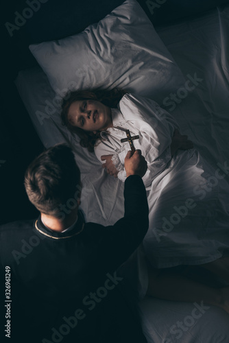 exorcist holding cross over obsessed girl in bed