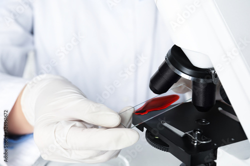 Scientist holding slide with blood sample near microscope in laboratory  closeup. Virus research