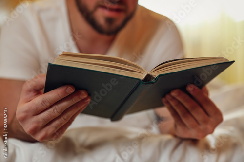 Young man reading book on bed at home, closeup