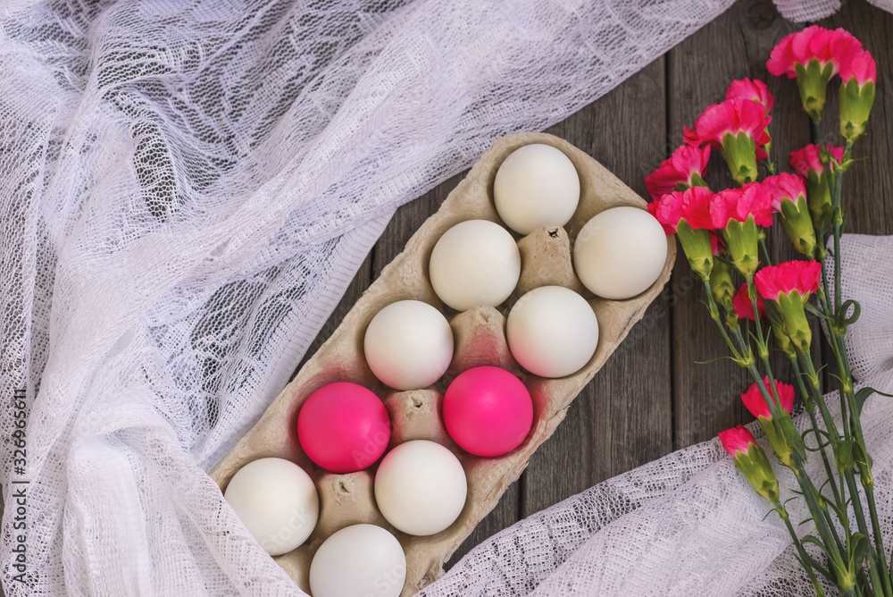 Happy Easter. White and pink chicken eggs, in a stand on a wooden background with red carnation flowers. Concept of holidays. Happy Easter. White and pink chicken eggs, in a stand on a wooden background with red carnation flowers. Concept of holidays.
