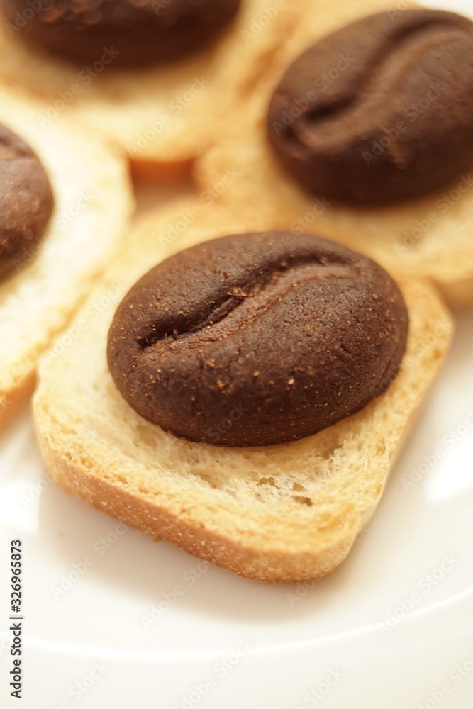 Brown cookies with shape of cocoa beans closeup in white plate.