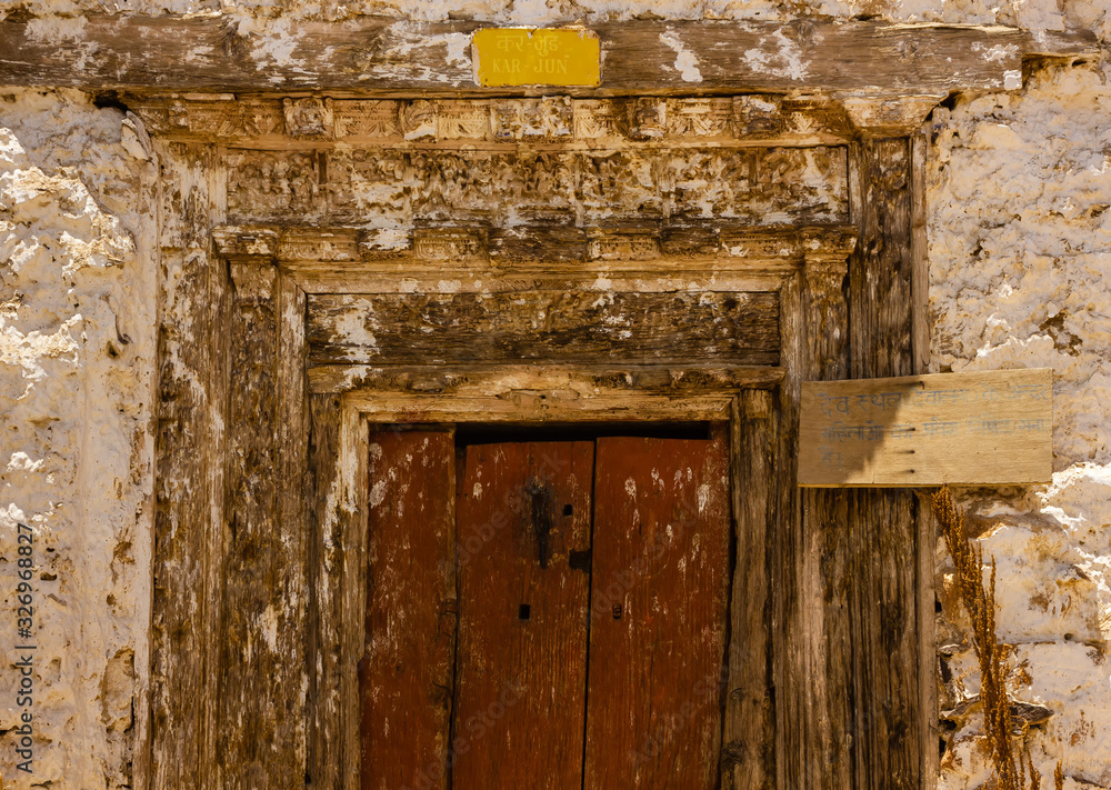 A wooden door to a shrine with faded carvings inside the ancient Buddhist monastery at Nako in Kinnaur, India. The text in Hindi says A wooden door to a shrine with faded carvings inside the ancient Buddhist monastery at Nako in Kinnaur, India. The text in Hindi says