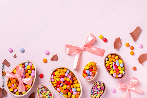 Chocolate Easter border with chocolate eggs and colorful candy sweets on pastel pink, copy space. Traditional Easter treats flat lay, holiday background
