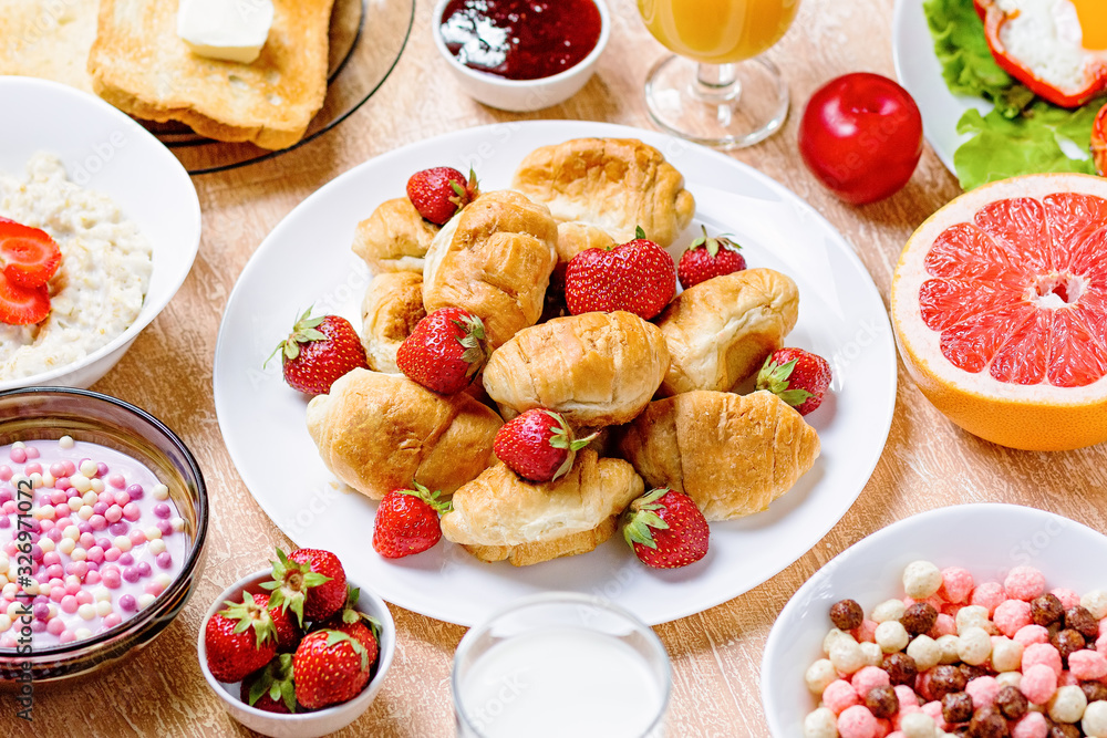 Continental breakfast with cereal, fried eggs, croissants, fruits and drinks on textured table, copy space. Table top with various healthy snacks and foods on rustic background Continental breakfast with cereal, fried eggs, croissants, fruits and drinks on textured table, copy space. Table top with various healthy snacks and foods on rustic background
