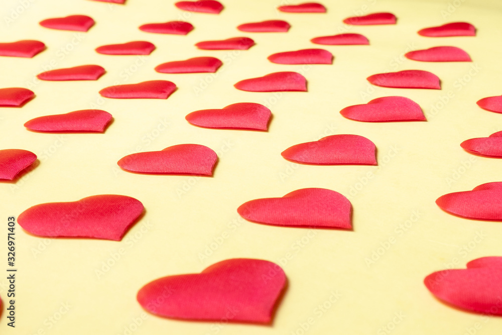 A lot of identical red silk hearts lying staggered on a yellow background. Symbol of love, tenderness and passion A lot of identical red silk hearts lying staggered on a yellow background. Symbol of love, tenderness and passion