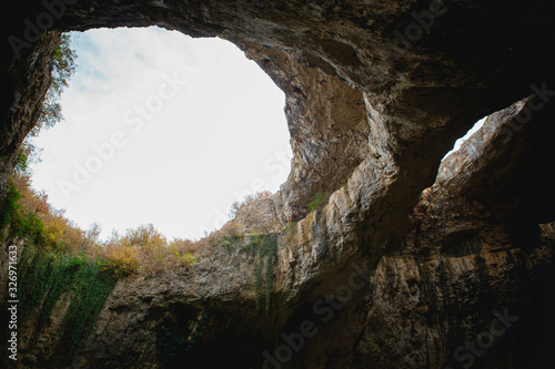 High arches of a huge stone cave with round holes at the top, a tourist road with a fence inside the cave. Bulgaria's natural attraction-Devetashka cave