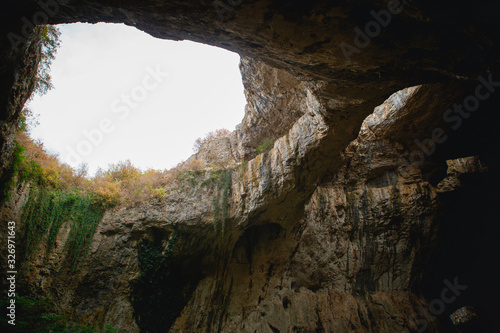 High arches of a huge stone cave with round holes at the top, a tourist road with a fence inside the cave. Bulgaria's natural attraction-Devetashka cave