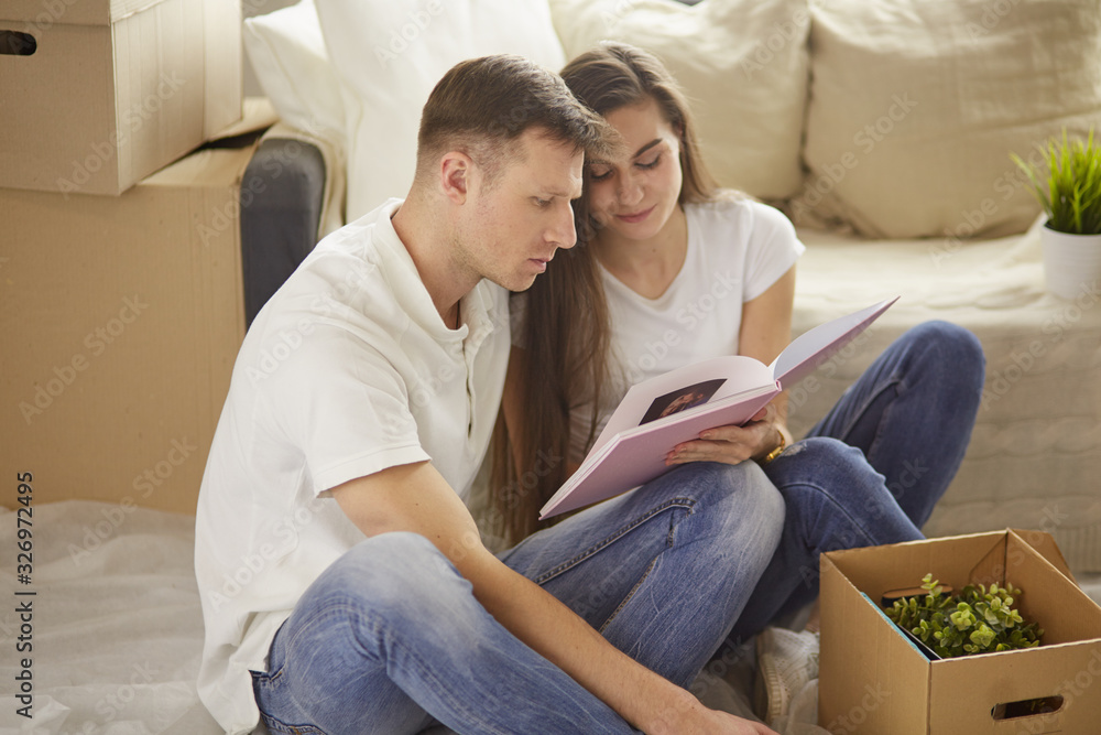 Portrait of happy couple looking at laptop computer together sitting in new house, surrounded with boxes Portrait of happy couple looking at laptop computer together sitting in new house, surrounded with boxes