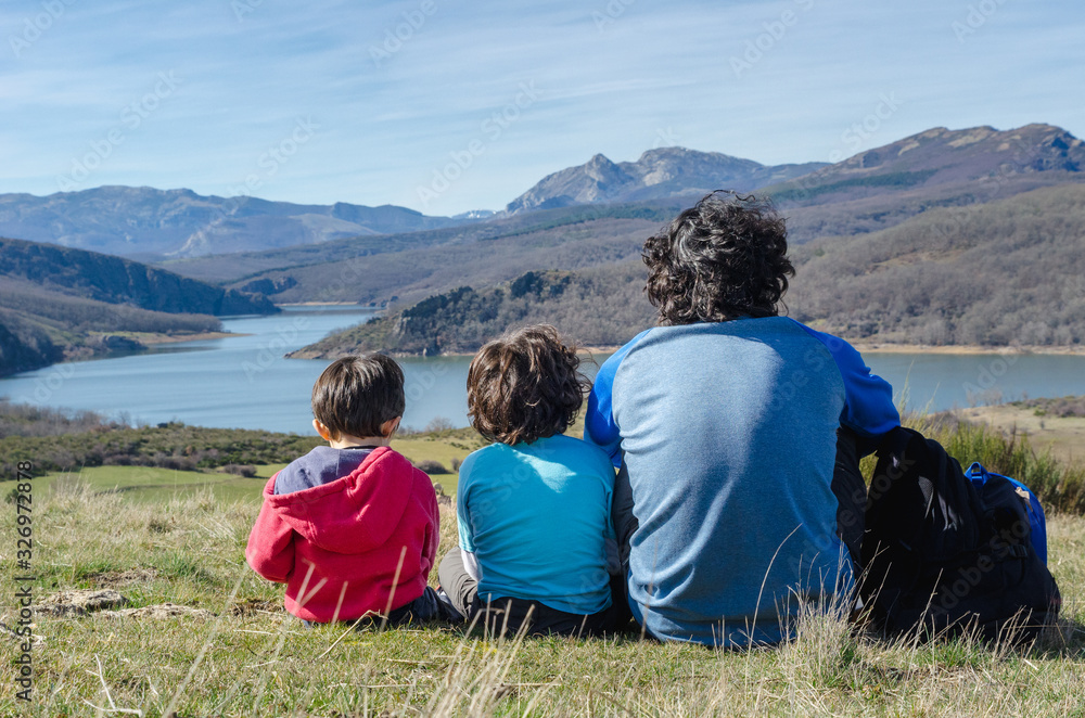 Fototapeta premium father and his two sons relaxing for a moment and enjoying the views after a hard hiking in the mountains of Palencia, Spain