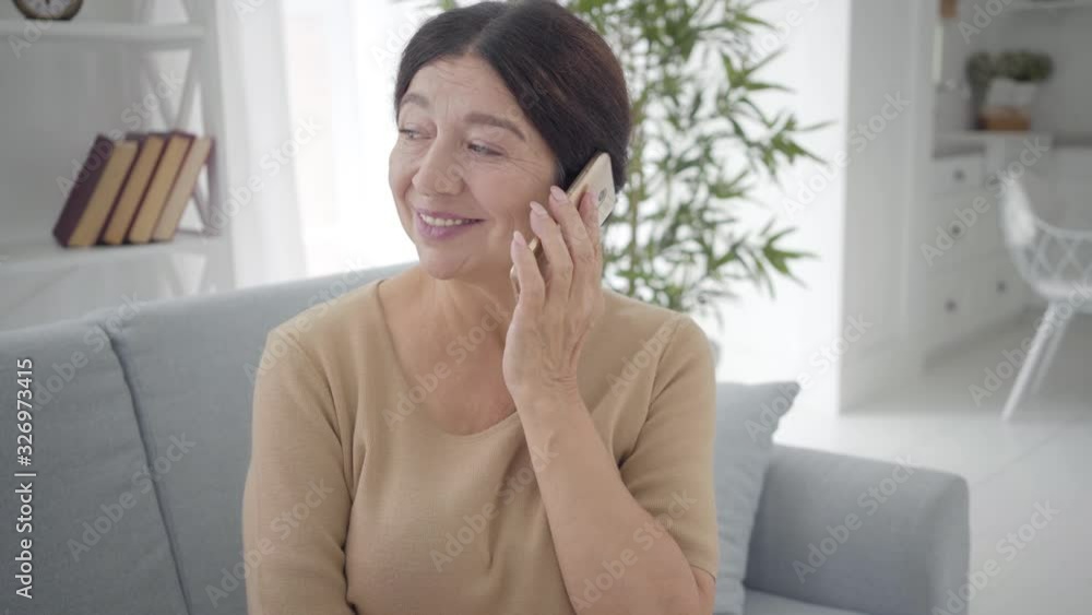 Portrait of beautiful senior Caucasian woman talking on the phone. Pleasant mature brunette lady with brown eyes chatting indoors. Lifestyle, beauty, tranquility. Portrait of beautiful senior Caucasian woman talking on the phone. Pleasant mature brunette lady with brown eyes chatting indoors. Lifestyle, beauty, tranquility.