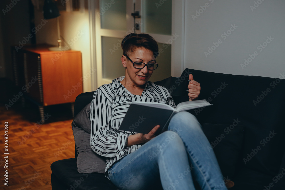 woman reading book, relaxed on sofa in her home. night evening scene