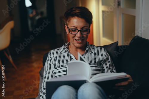 woman reading book, relaxed on sofa in her home. night evening scene