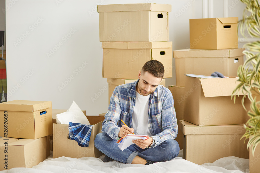 Handsome man with boxes in the new apartment after moving Handsome man with boxes in the new apartment after moving