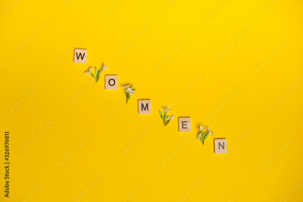 Top view word women spelled in wooden blocks on yellow background with flowers between them. Love, 8 march background. Gift, greeting, compliment concept. Copy space. place for text. Top view word women spelled in wooden blocks on yellow background with flowers between them. Love, 8 march background. Gift, greeting, compliment concept. Copy space. place for text.