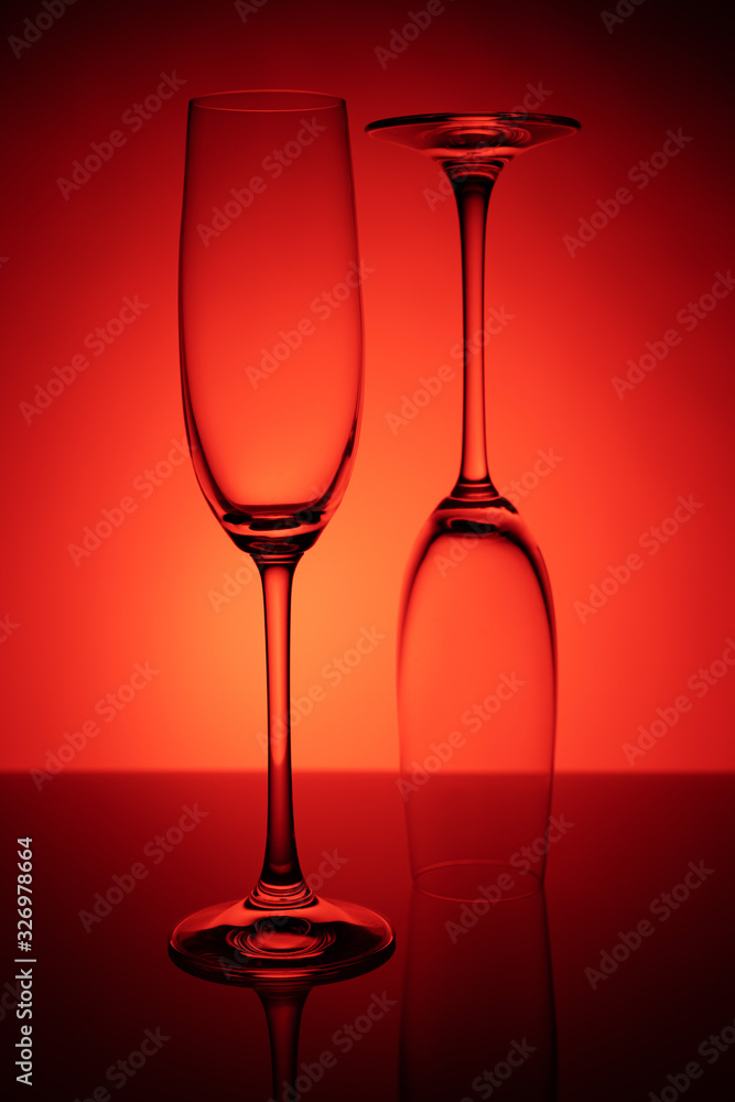 Two empty glasses of champagne with reflection, on a red and black background gradient background. Concept, party and club life. Two empty glasses of champagne with reflection, on a red and black background gradient background. Concept, party and club life.