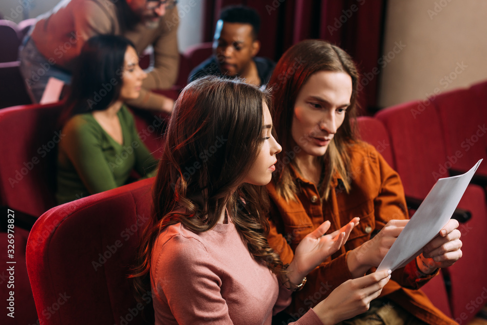 young actor and actress reading screenplay on seats with others