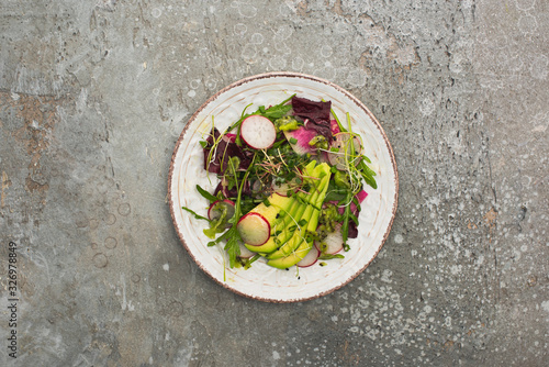 top view of fresh radish salad with greens and avocado on grey concrete surface