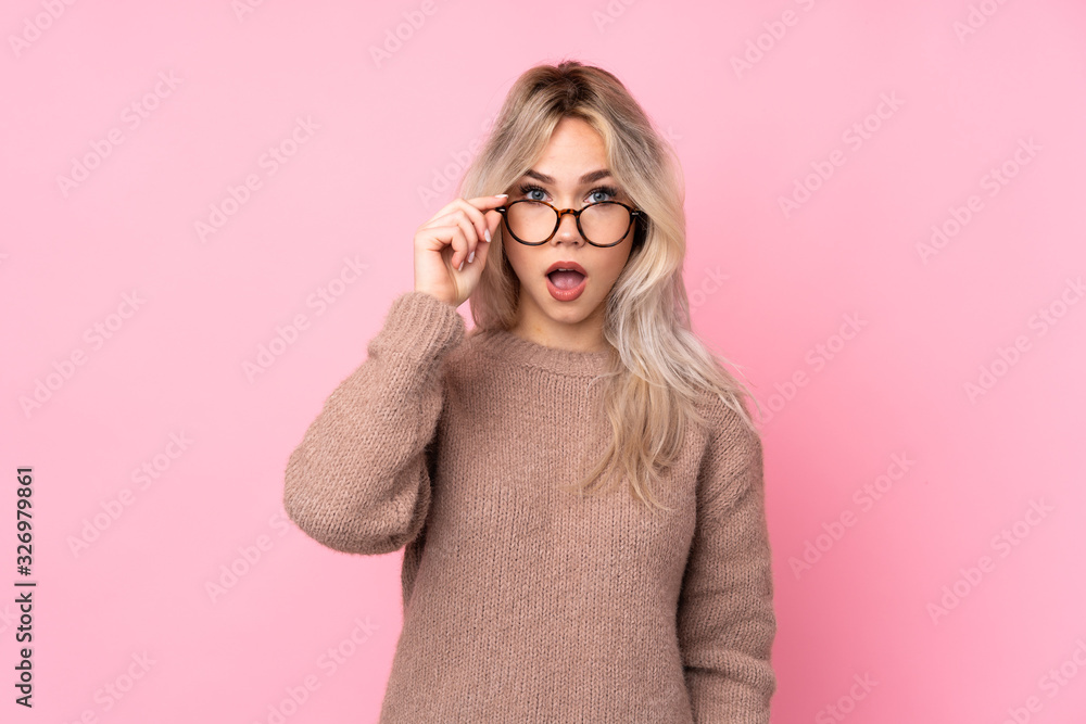 Teenager blonde girl wearing a sweater over isolated pink background with glasses and surprised Teenager blonde girl wearing a sweater over isolated pink background with glasses and surprised