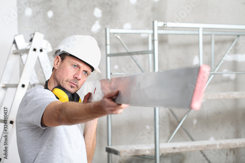 man work,  checks the straightedge to level the wall, with ladder and scaffolding in the interior construction site on background photo